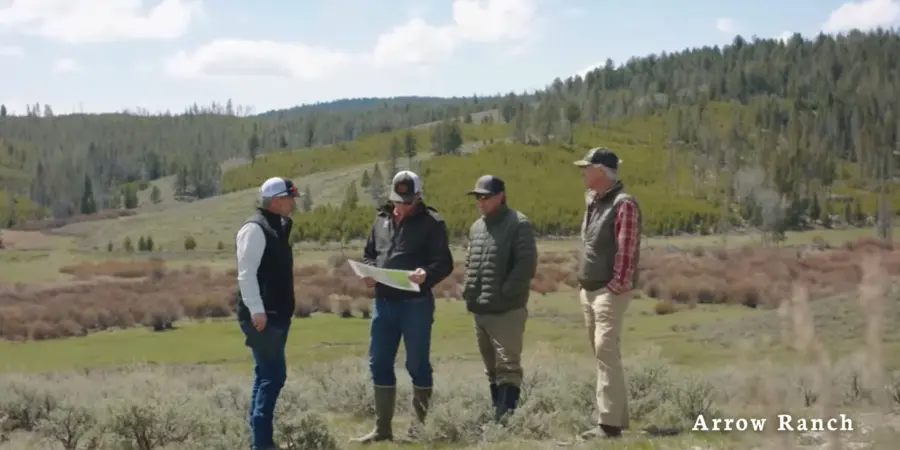 Four men in outdoor clothing stand in a grassy field with hills and trees in the background, reviewing a map. The words Arrow Ranch appear in the lower right corner.
