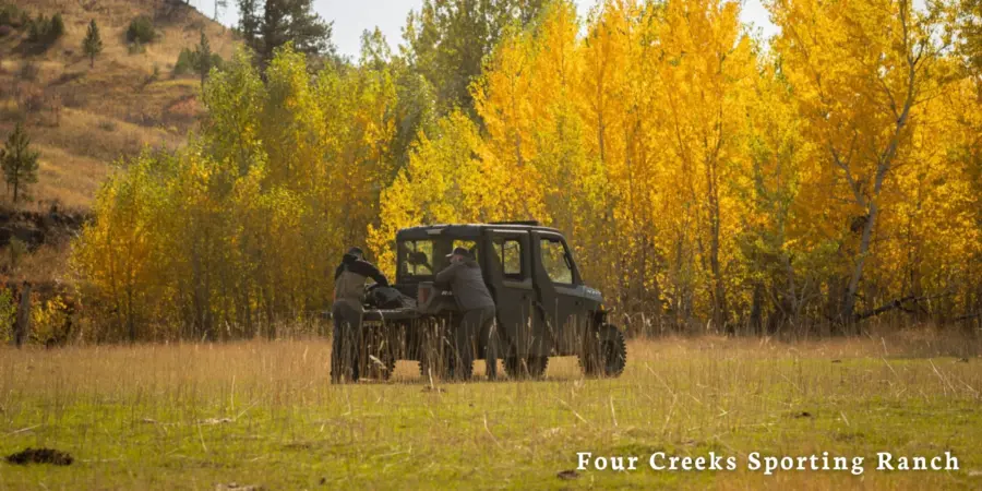 Two people stand beside an off-road vehicle in a grassy field with trees displaying vibrant yellow autumn foliage. Text reads Four Creeks Sporting Ranch in the lower right corner.